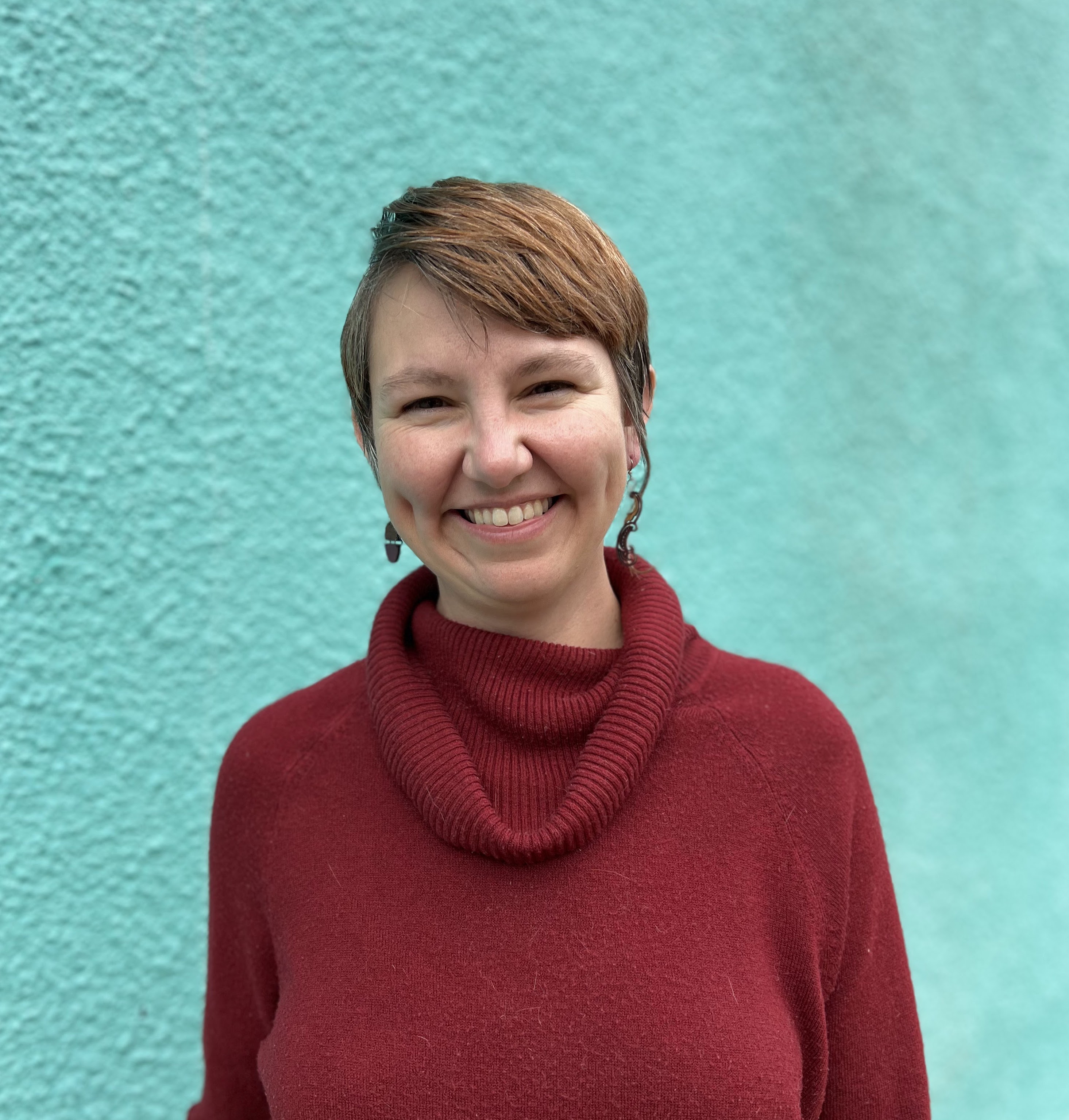 Andi Cheney in a red sweater smiles in front of a turquoise wall